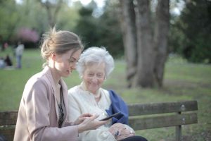 Senior woman with a younger female on a park bench, looking at her phone.